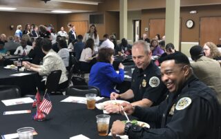 Several groupd sit at tables for the luncheon, including two members of local police enjoying a meal.