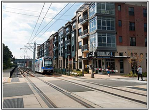 A street with a metro public tram line going by rosa of apartments and shops.