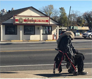 A homeless man on a wheelchair on a corner.